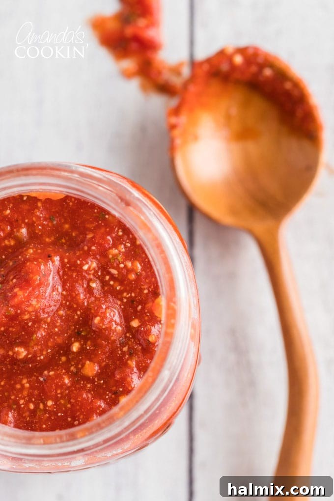 close up of jar of homemade pizza sauce with a spoon on the side
