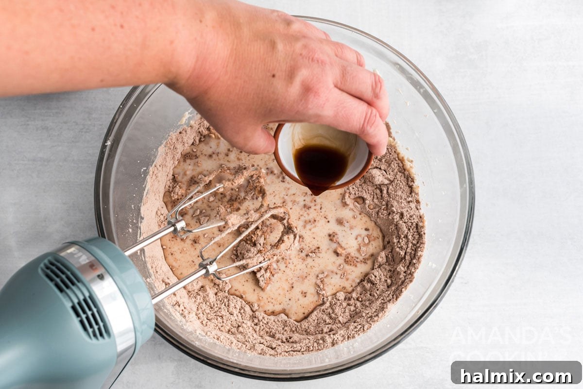 Pouring vanilla extract into the mixer bowl with whoopie pie dough, highlighting the addition of aromatic flavors.