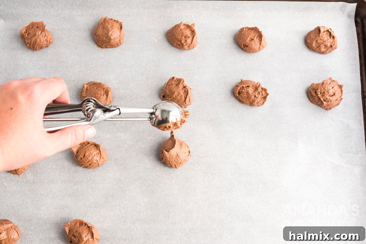 Scooping small portions of whoopie pie dough onto a parchment-lined cookie sheet, ensuring even spacing for perfect mini cookies.