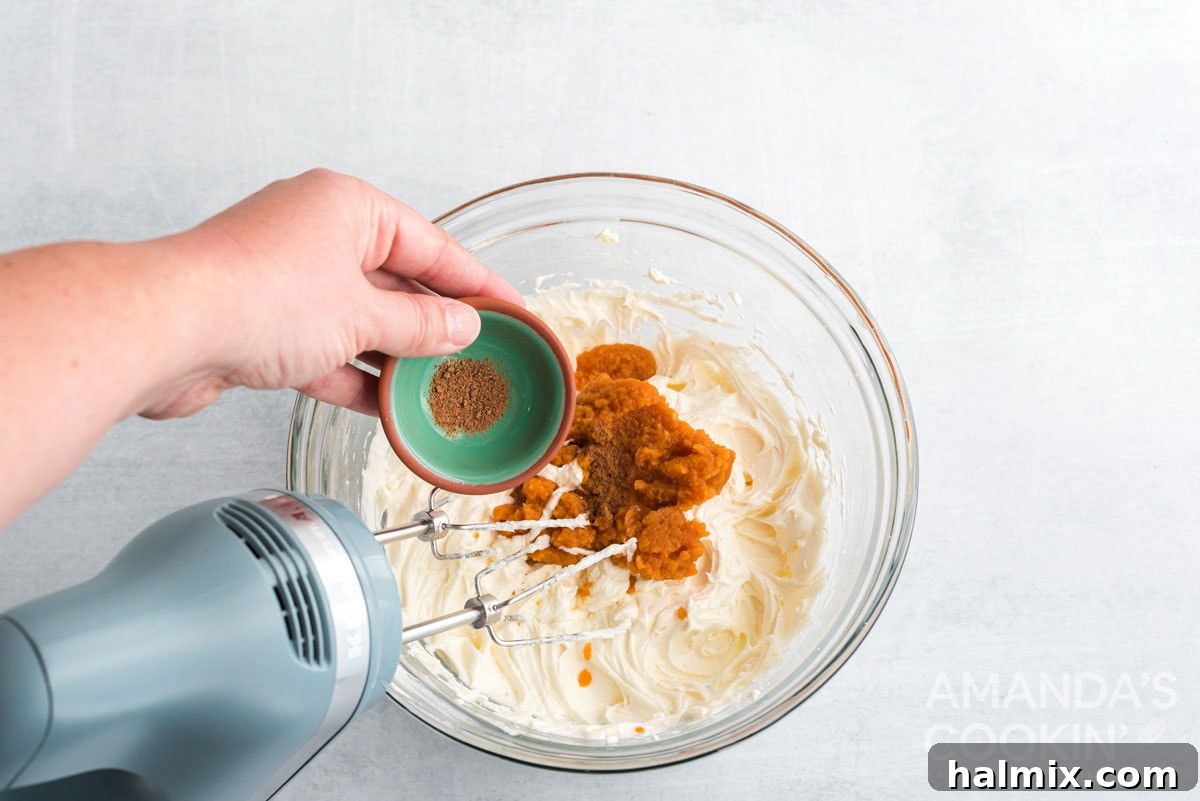 Adding warm spices like cinnamon and nutmeg to the pumpkin cream cheese filling mixture in a mixing bowl, enhancing its fall flavor.