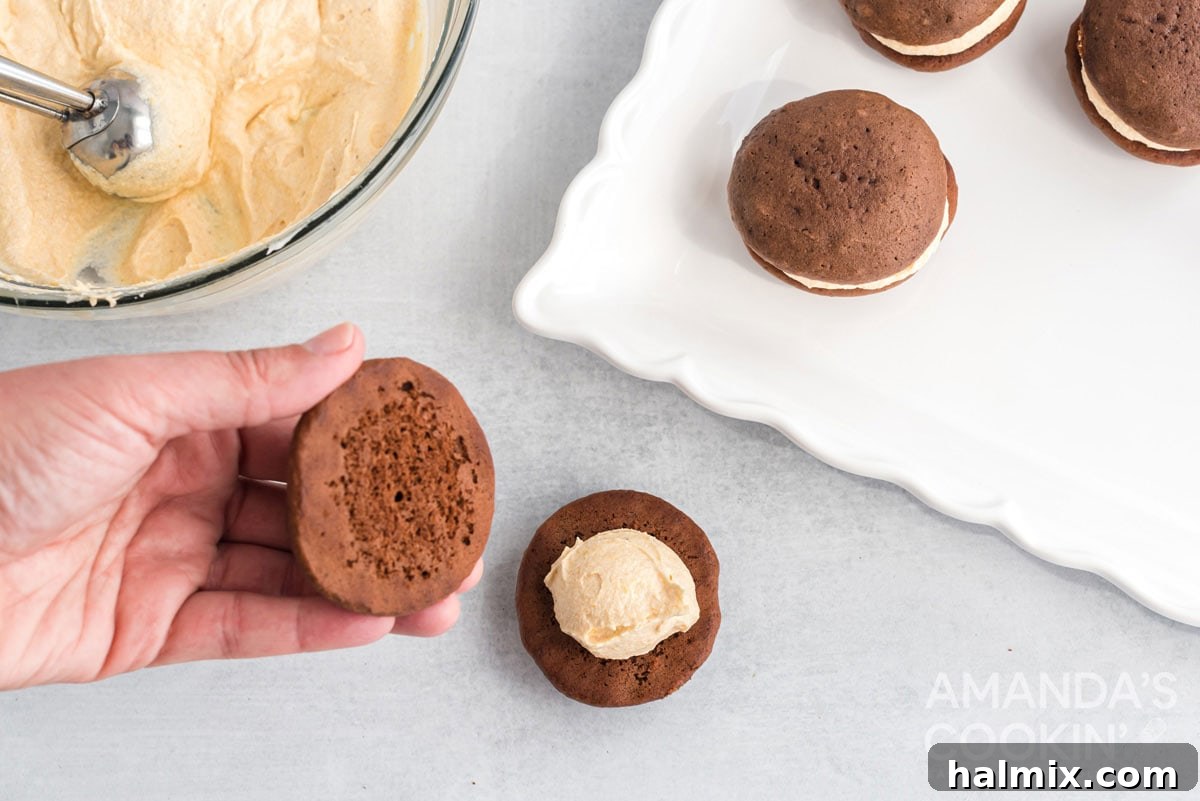Assembling a mini pumpkin whoopie pie by placing the top cookie onto the creamy filling, creating a perfect sandwich dessert.