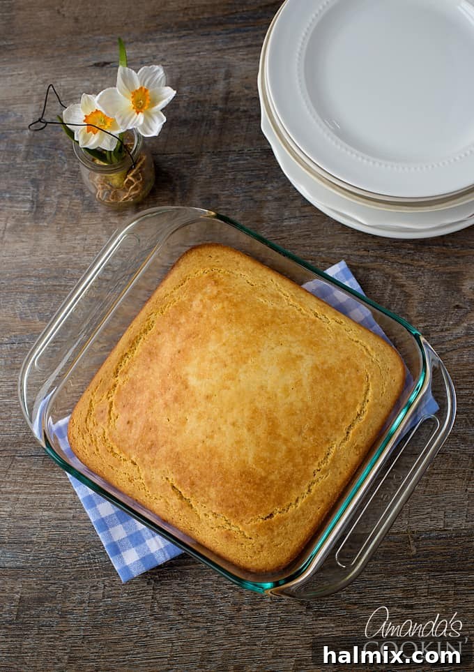 Delicious Sweet Cornbread 3 A freshly baked pan of golden sweet cornbread resting on a blue checkered towel, ready to be sliced and served.