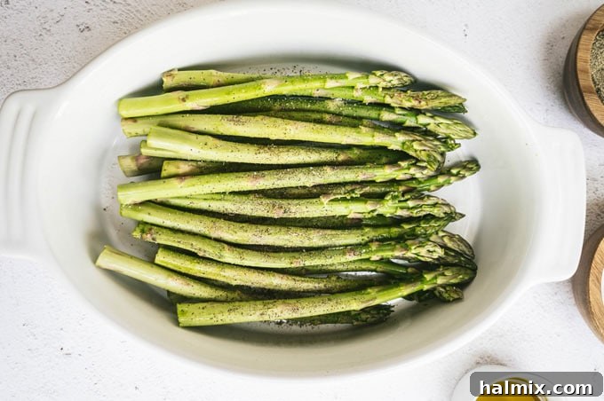 raw asparagus in a white dish, surrounded by small bowls of olive oil, kosher salt, and black pepper