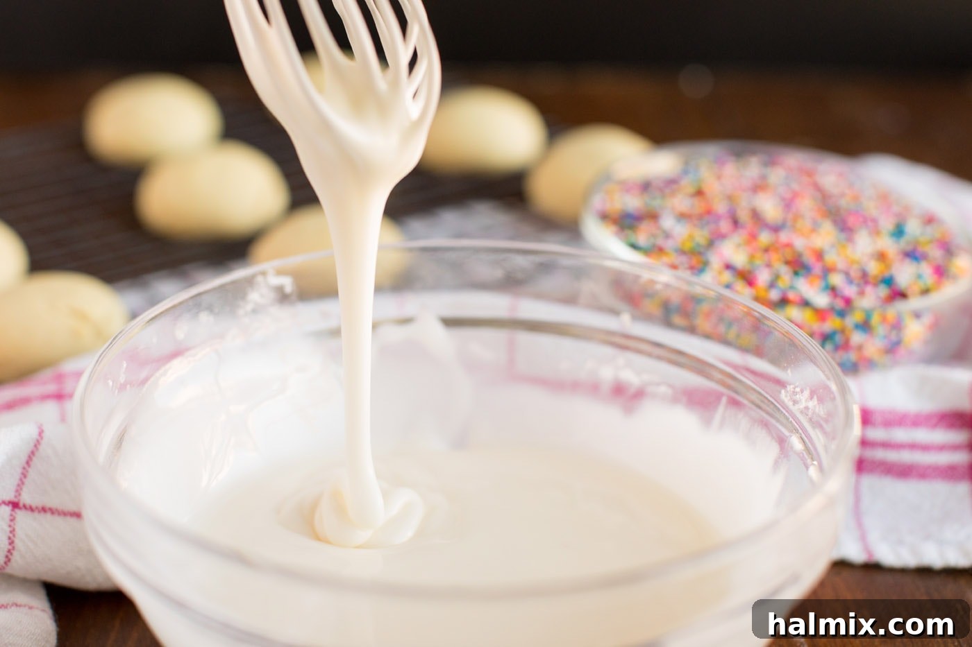 Thick glaze being lifted with a whisk, demonstrating the ideal consistency for dipping cookies.