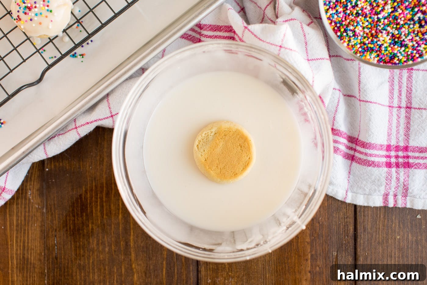 A cookie being dipped into the white glaze, showing the even coating.