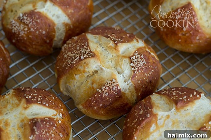A close-up view of golden-brown bretzel rolls, lightly salted, resting on a wire cooling rack.