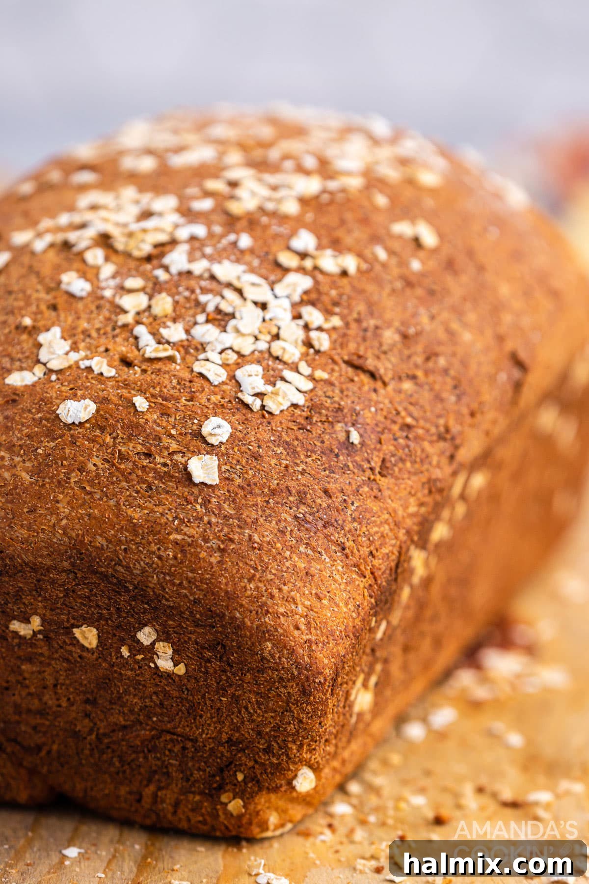 A close-up view of a whole, unsliced loaf of homemade multigrain bread, showcasing its textured crust and sprinkle of oats.