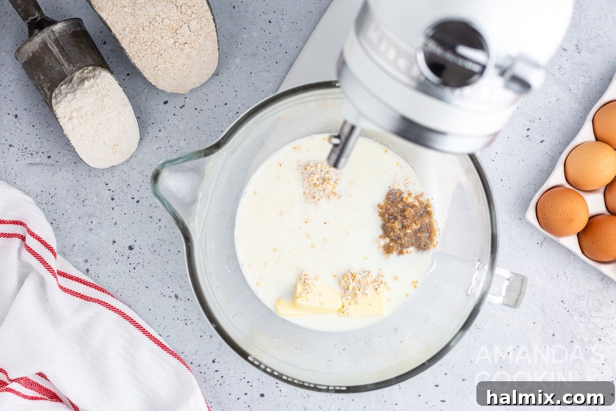 Warm milk combined with oatmeal, sugar, butter, and salt in a stand mixer bowl, ready for the next ingredients.