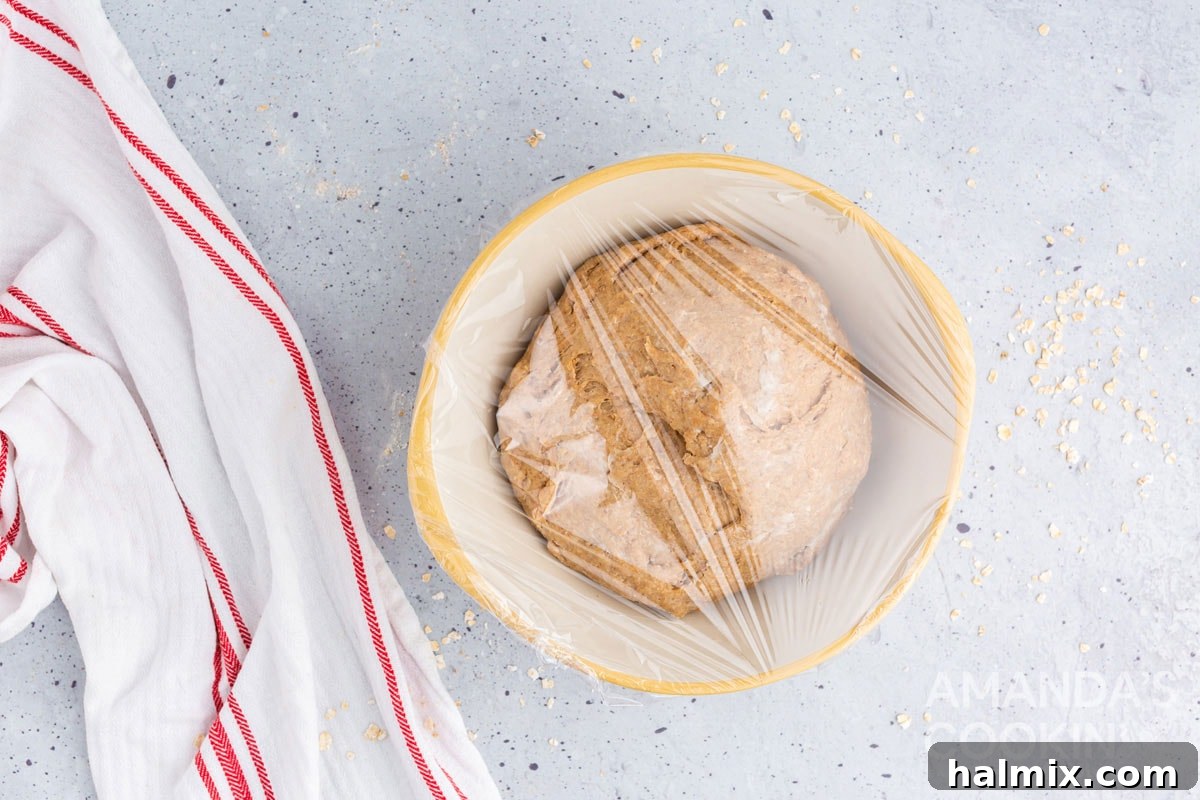 A bowl of freshly prepared bread dough, generously buttered and covered tightly with plastic wrap, set aside for its first rise.