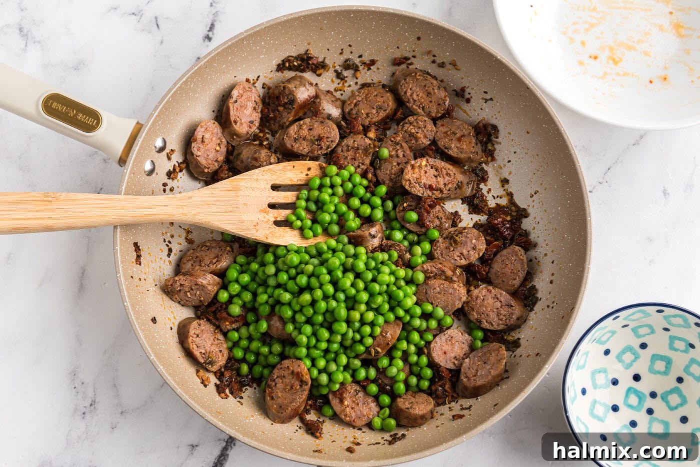 green peas added to Italian sausage and sun dried tomatoes in a skillet