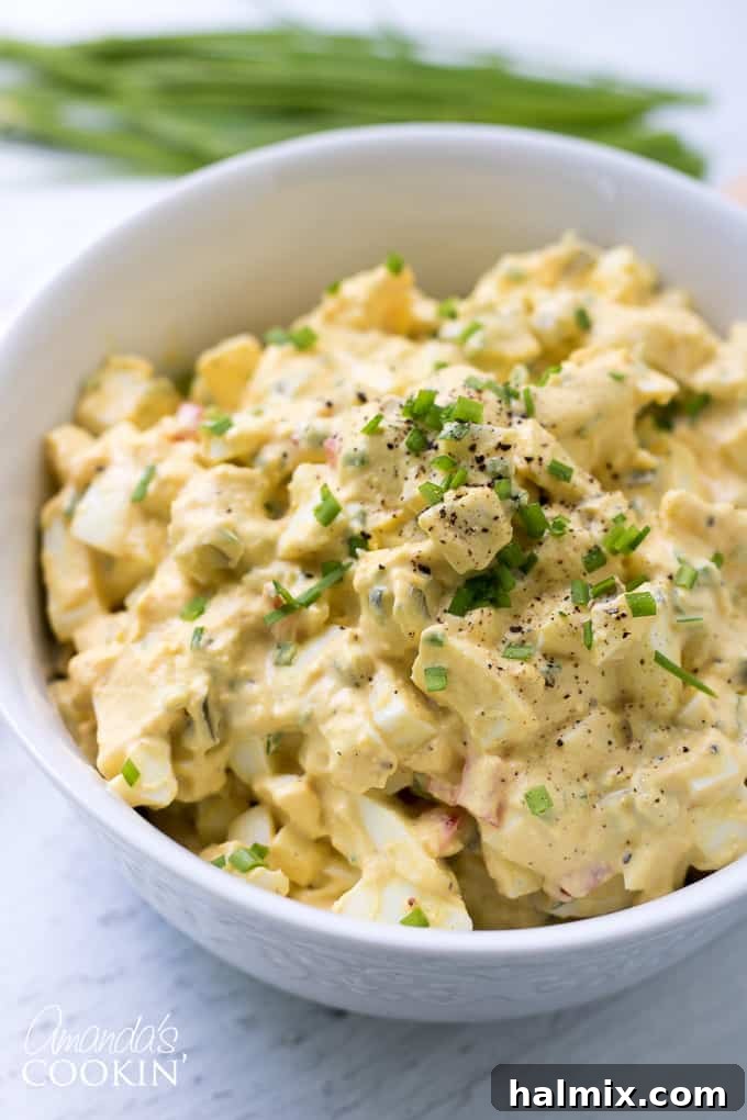 A bowl of creamy homemade egg salad, beautifully topped with fresh green chives, perfectly prepared for serving. A simple yet elegant dish.
