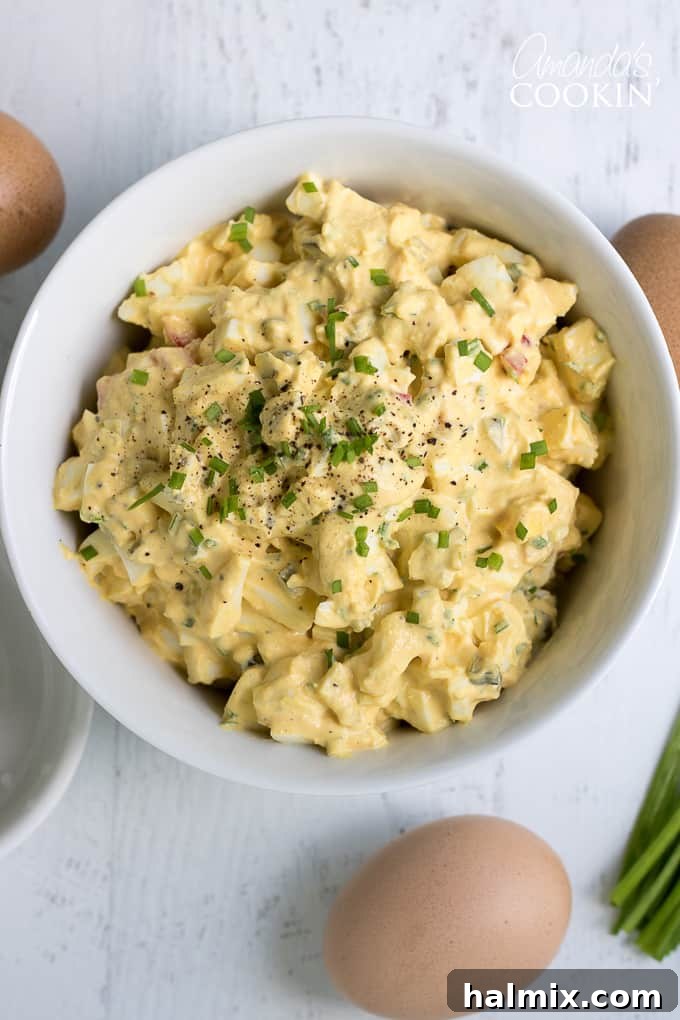 Close-up of freshly made Egg Salad, showcasing its creamy texture with visible pieces of chives and red bell pepper, ready to be enjoyed.