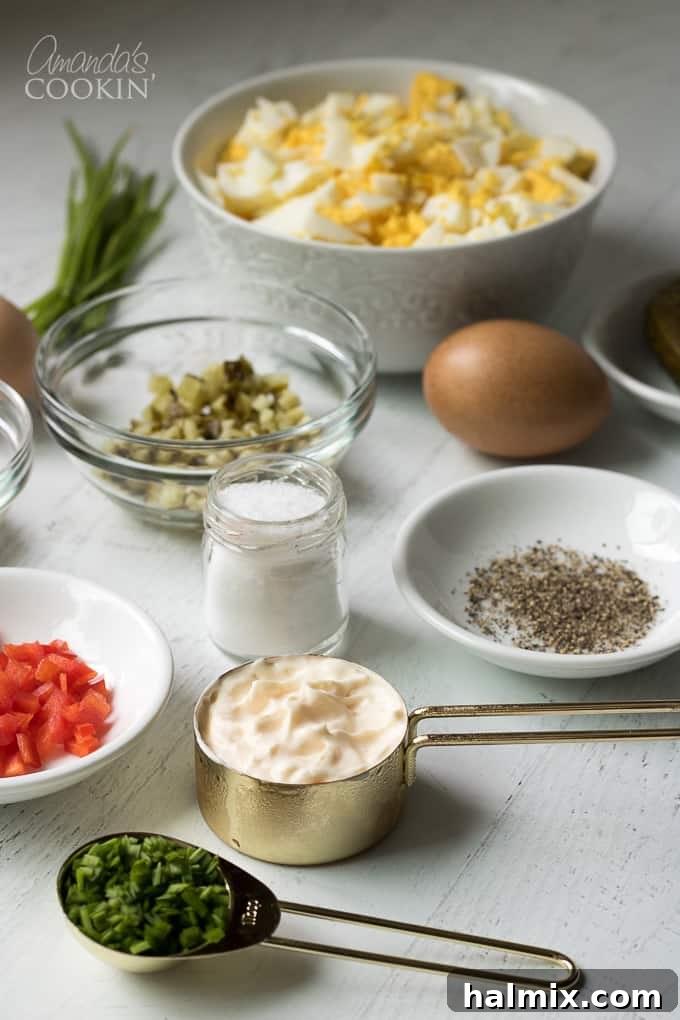 A vibrant flat lay photograph displaying all the fresh ingredients required for making classic egg salad: hard-boiled eggs, mayonnaise, Dijon mustard, a dill pickle, red bell pepper, and fresh chives.