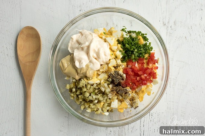 All the egg salad ingredients, including chopped hard-boiled eggs, mayonnaise, and fresh vegetables, are brought together in a mixing bowl, ready for combining.