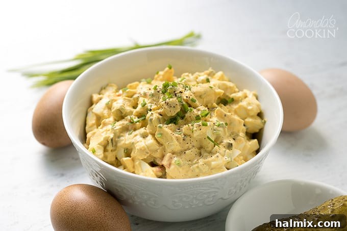 A generously sized bowl of creamy egg salad with fresh chives, presented beautifully and ready to be served, accompanied by an array of fresh bread and crackers. Perfect for sharing at any gathering.