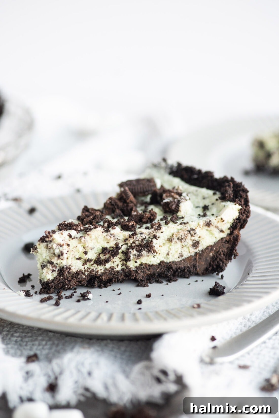 Emerald Mint Delight 11 A perfectly sliced piece of Grasshopper Pie, showing the distinct layers of chocolate crust, vibrant green mint filling, and Oreo crumble topping.