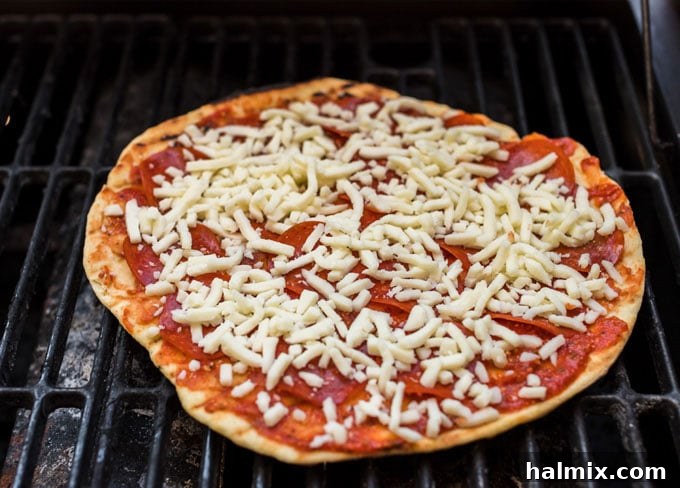 A topped pizza cooking on the center rack of a gas grill, with flames visible from the outer burners, demonstrating indirect heat cooking.