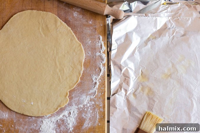 Four pieces of raw pizza dough, each placed on an oiled aluminum foil sheet, stacked and ready for grilling.