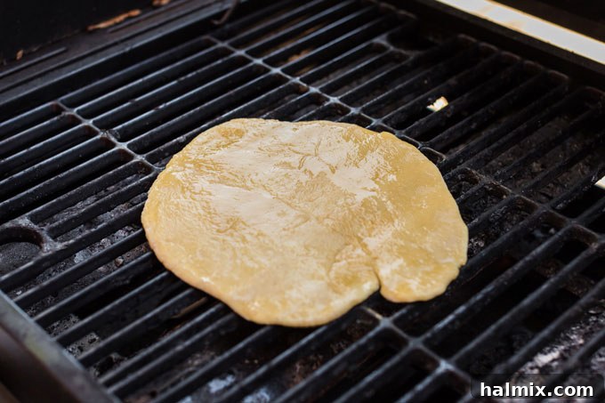 A raw pizza dough circle beginning to cook on a gas grill, showing slight puffiness and early grill marks.