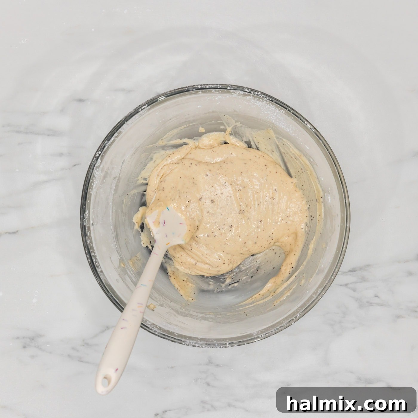 Smooth brown butter glaze in a bowl, stirred with a rubber spatula, ready to be poured over the cake.