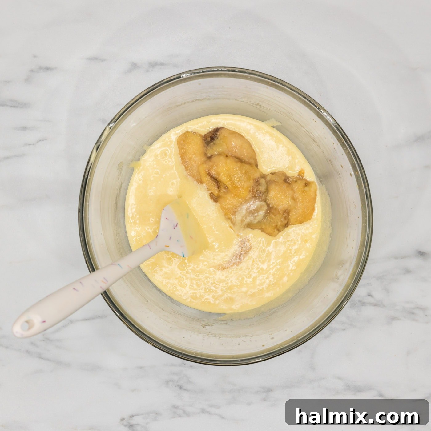 Mashed bananas added to the bundt cake batter in a bowl, ready for mixing.