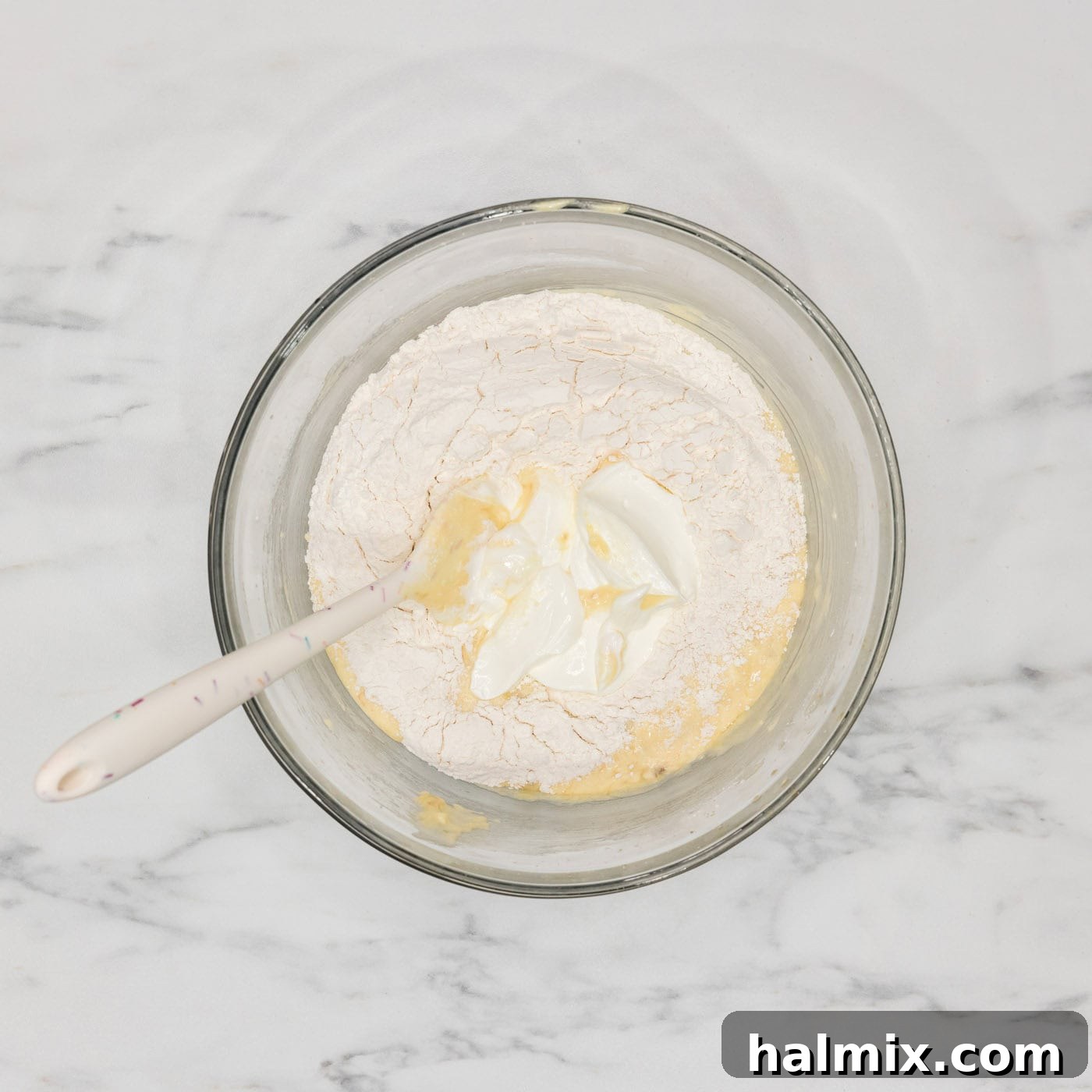 Adding dry ingredients to the sour cream and wet ingredients for the bundt cake batter, demonstrating the alternating method.