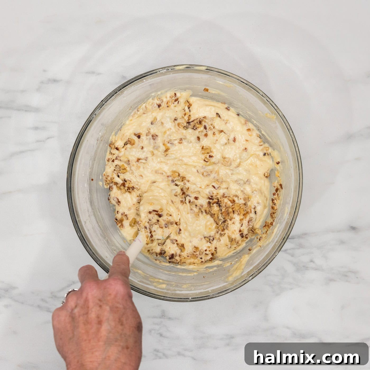 Stirring walnuts into the bundt cake batter in a bowl, ensuring even distribution.