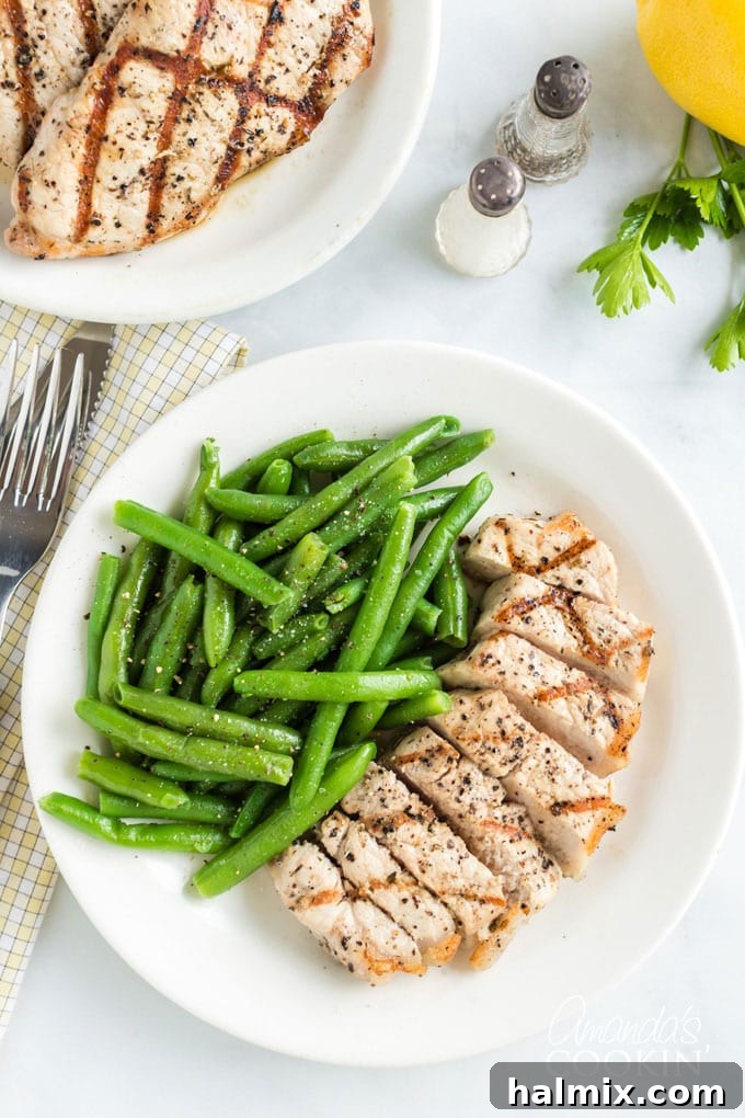 Learn how to make the perfect grilled pork chops. My go-to marinade is very easy and includes lemon juice, olive oil, garlic and a few fresh herbs. sliced pork chop on a plate with green beans