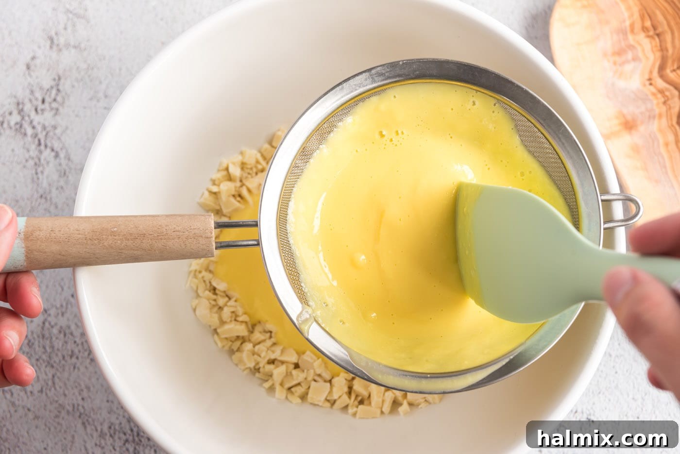 Custard` being strained over chopped white chocolate