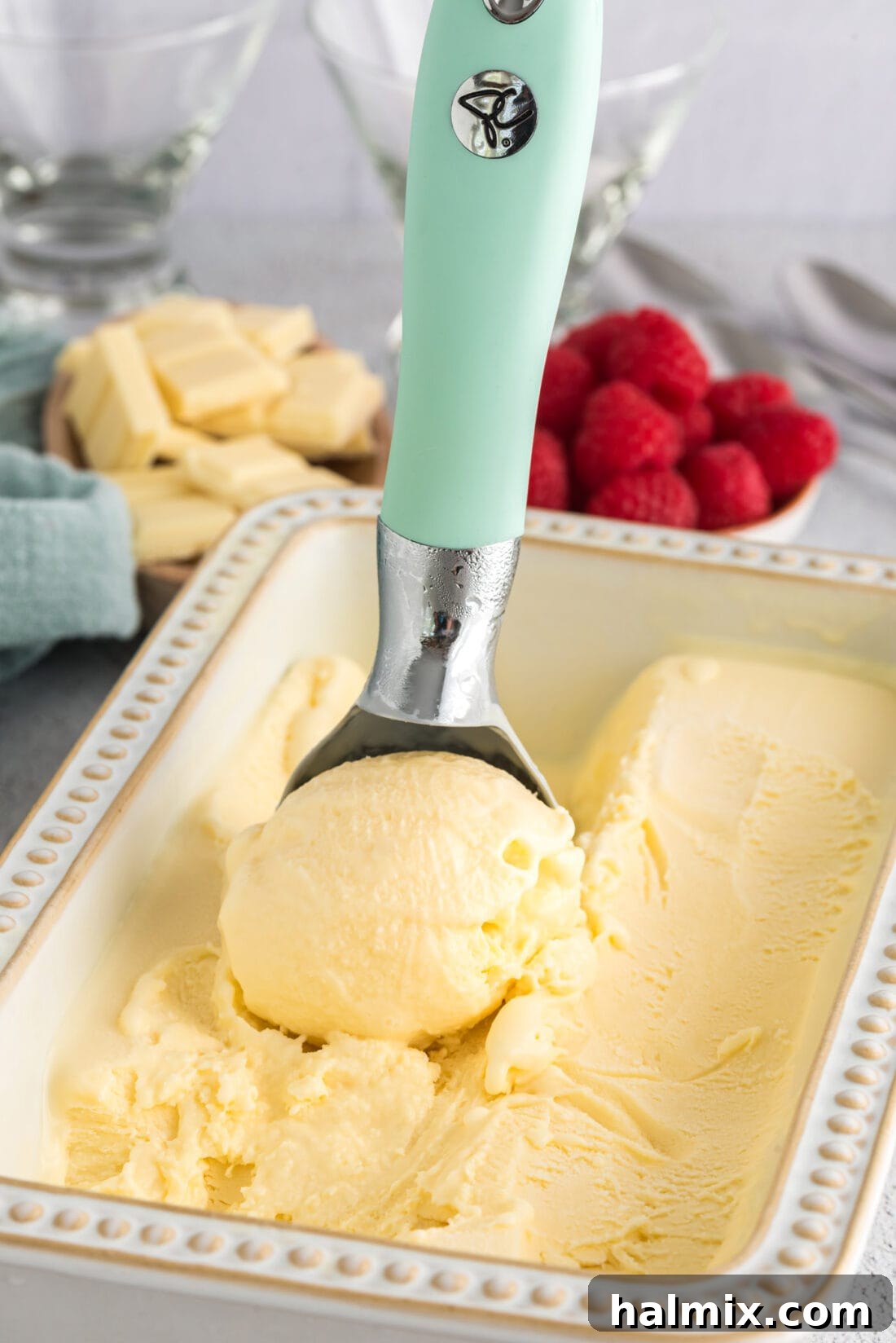 Ice cream scooper with a scoop of White Chocolate Ice Cream in a pan of White Chocolate Ice Cream