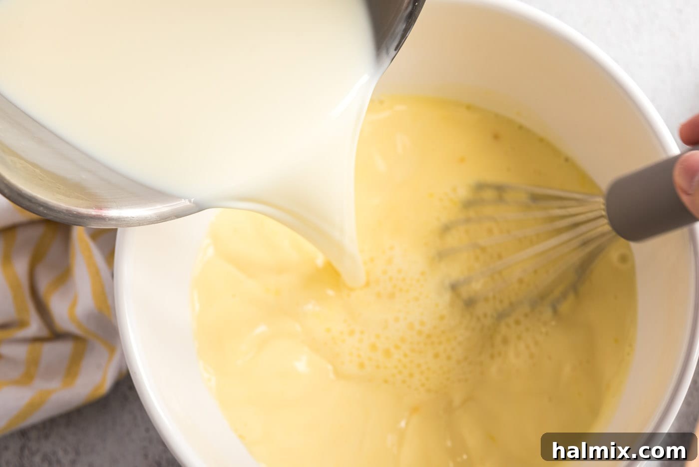 Milk mixture being poured into the whisked egg yolks