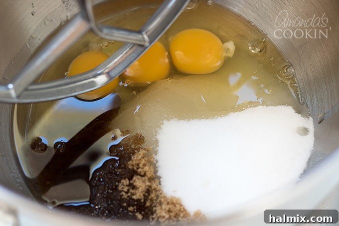 Mixing Wet Ingredients for Chocolate Zucchini Bread Batter Oil, white sugar, brown sugar, and eggs being beaten together in a stand mixer bowl until fluffy.