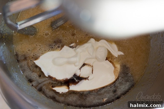 Adding Sour Cream and Vanilla to Zucchini Bread Batter Vanilla extract and sour cream being added to the wet ingredients in a mixer for chocolate zucchini bread.