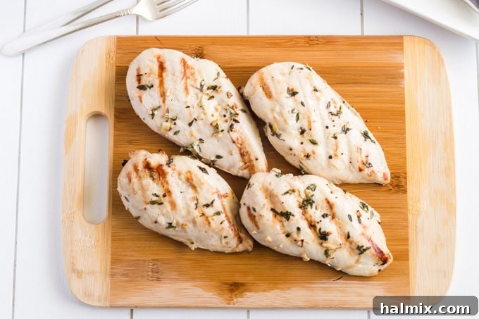 Cooked grilled chicken breasts, resting on a cutting board, ready to be sliced and served.