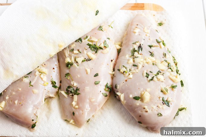 Marinated chicken breasts being patted dry with paper towels, removing excess marinade before grilling.