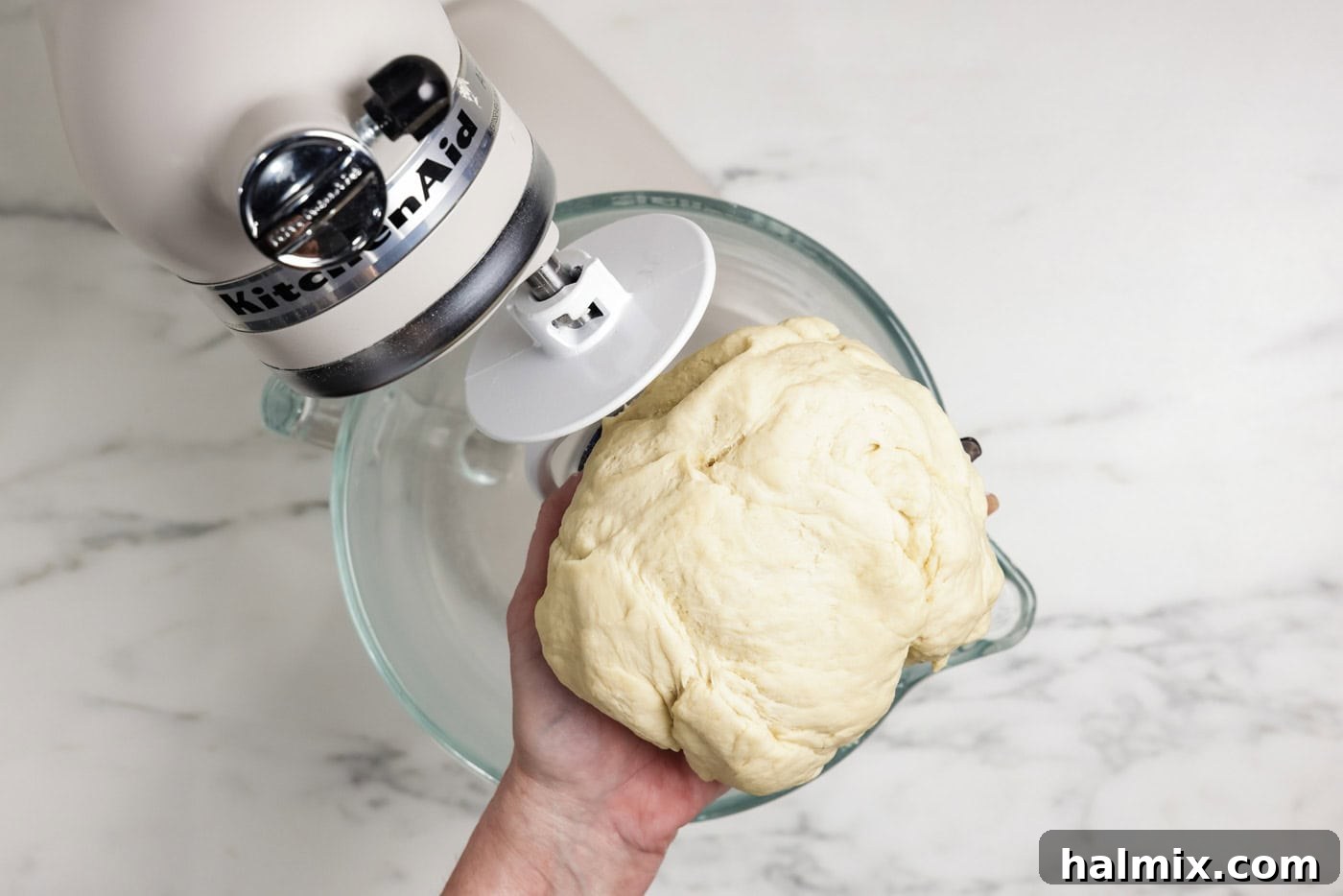 The 60-Minute Loaf 6 Hand holding bread dough over a stand mixer, showcasing the dough hook in action