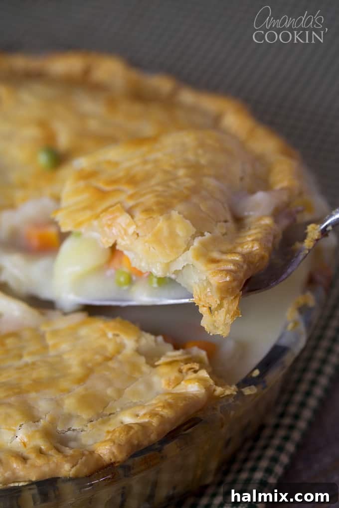 A close up of a spoonful of homemade turkey or chicken pot pie, showing the creamy filling and golden crust.