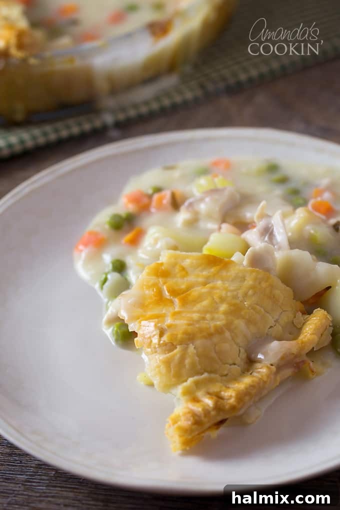 A close up of a serving of homemade pot pie on a white plate, showcasing the golden crust and rich filling.