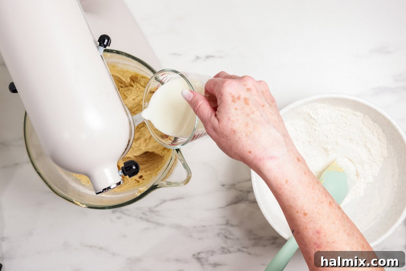 Pouring buttermilk into cookie dough in a mixer