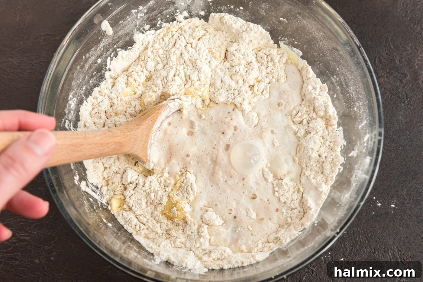 Stirring the flour, yeast, and butter mixture with a wooden spoon to form a dough.