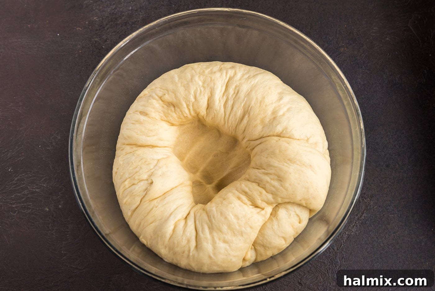 Gently punching a hole into the risen yeast dough to deflate it.