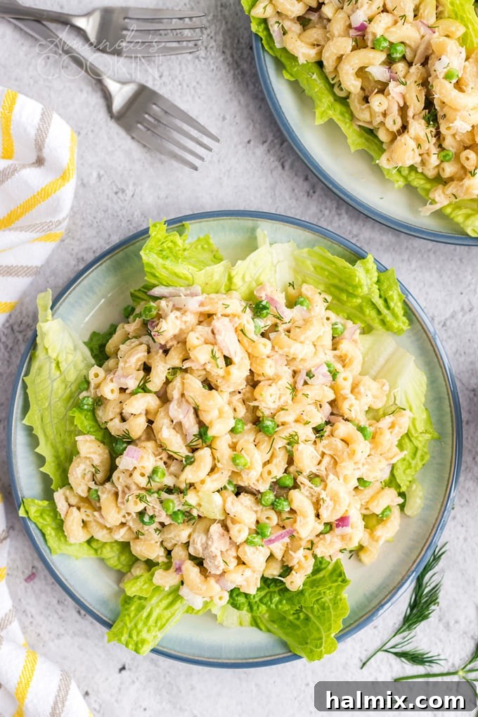 A vibrant bowl of creamy tuna pasta salad resting on a bed of fresh green lettuce, garnished with parsley.