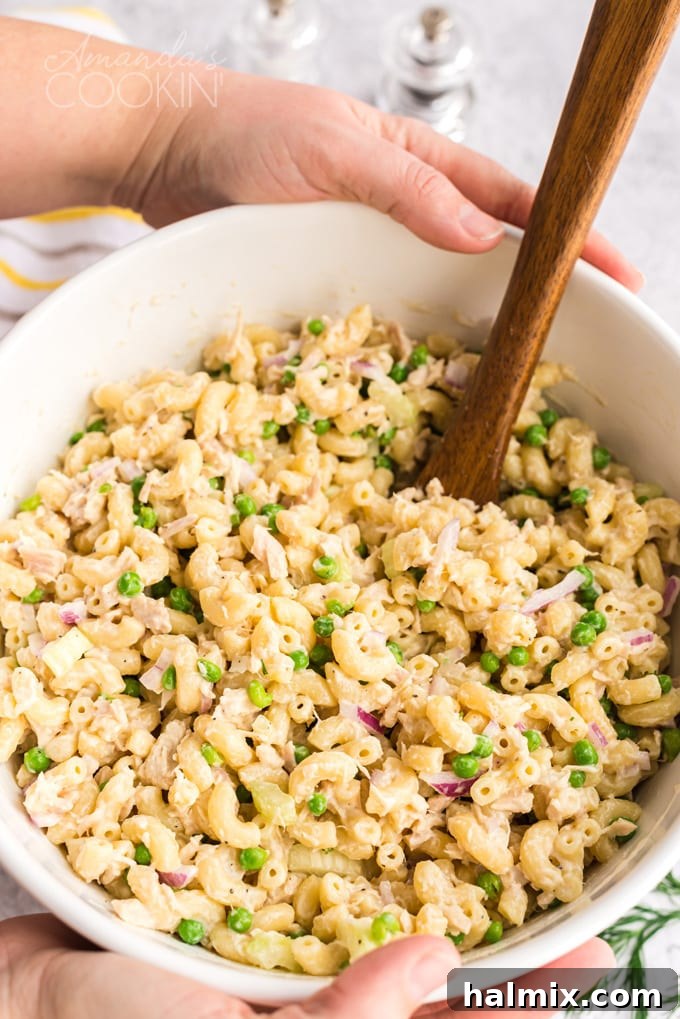 Someone's hands holding a large white bowl filled with freshly made tuna pasta salad, ready to be served.