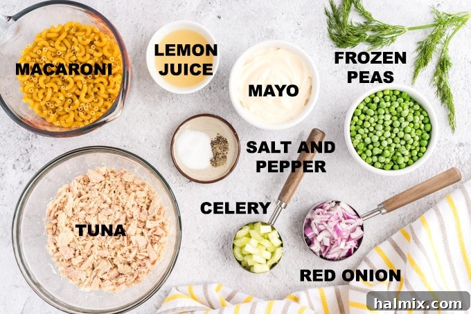 Fresh ingredients laid out on a table, including elbow macaroni, canned tuna, celery, red onion, frozen peas, mayonnaise, and a lemon.