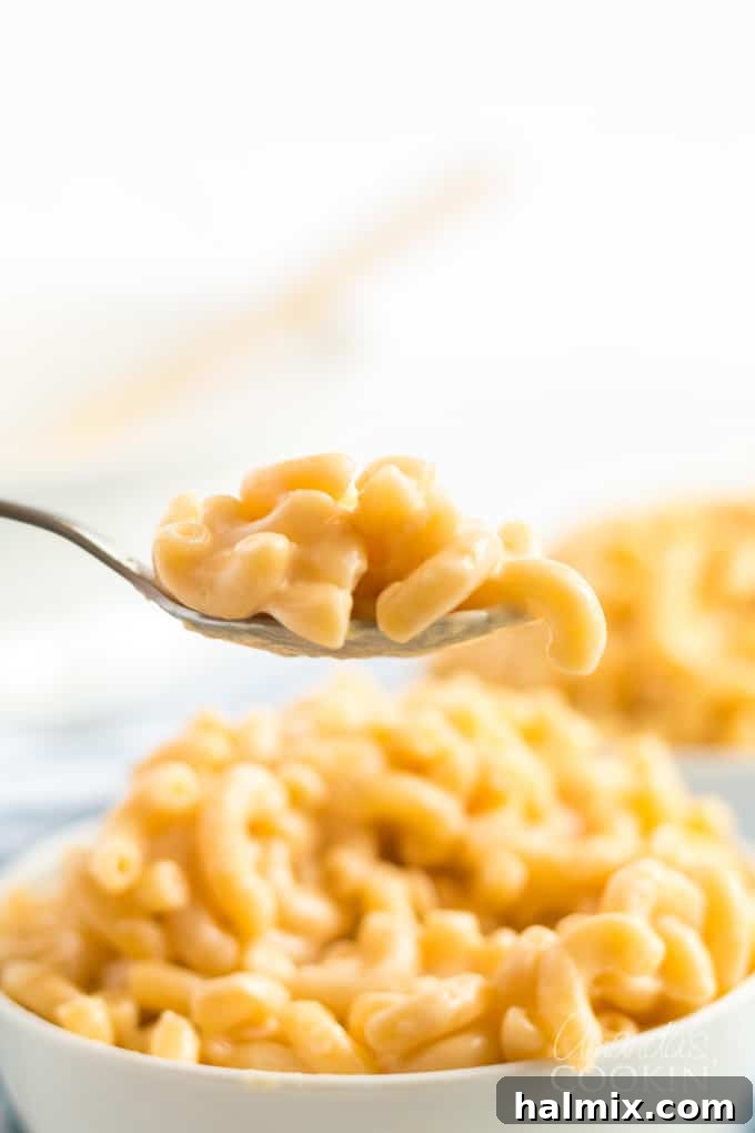 A spoonful of rich, creamy stovetop macaroni and cheese being lifted from a bowl.