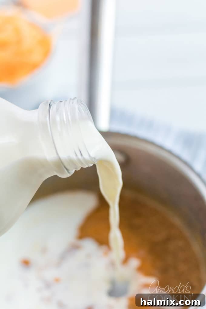 A close-up shot of milk being poured into a saucepan with roux, starting the cheese sauce for macaroni and cheese.