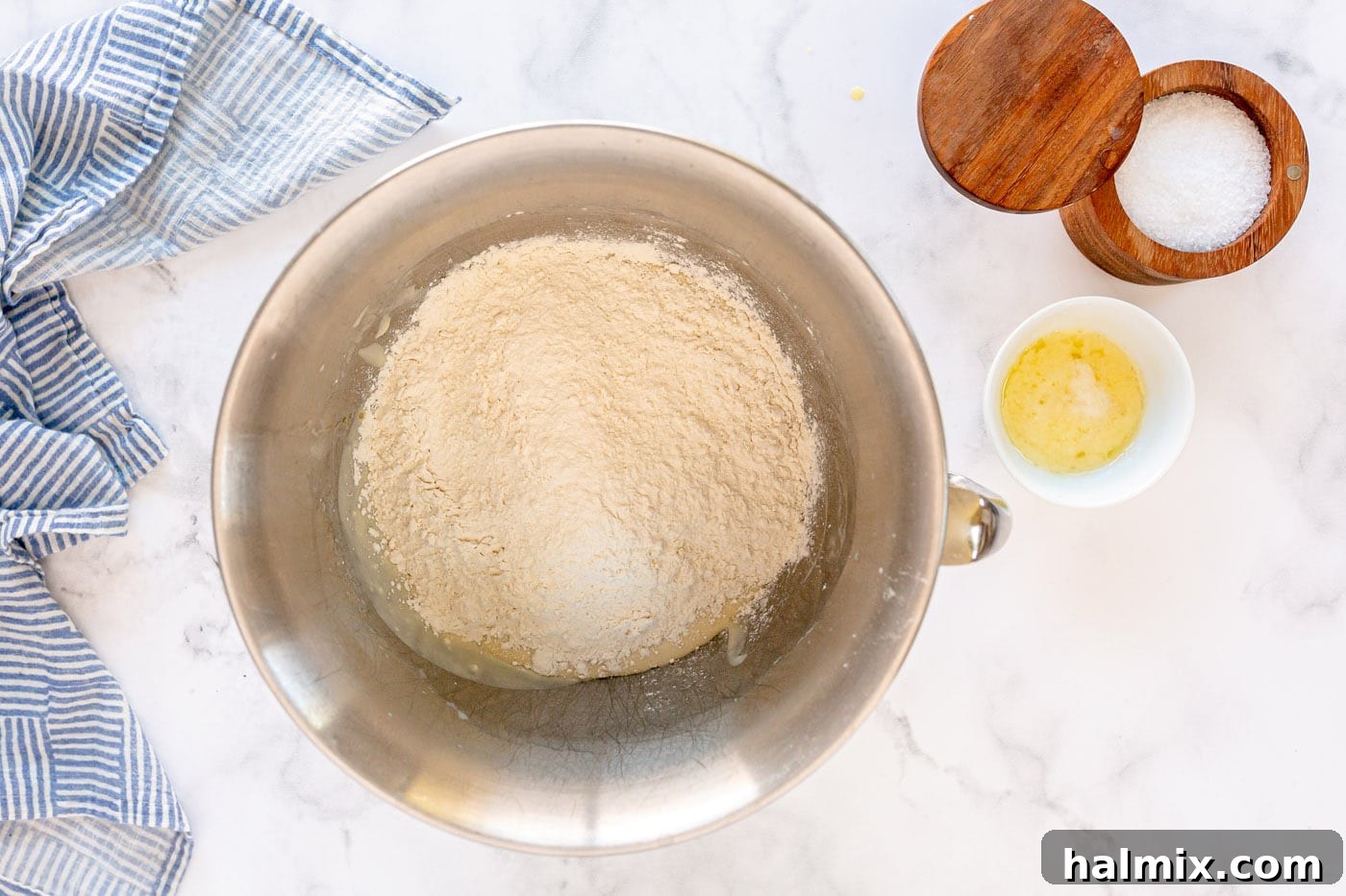 Flour being added to the mixing bowl to form the dough for dinner rolls.