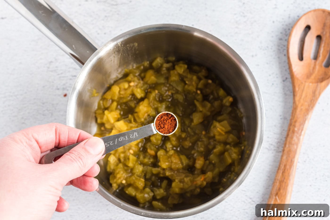 adding chile powder to green chiles in a saucepan