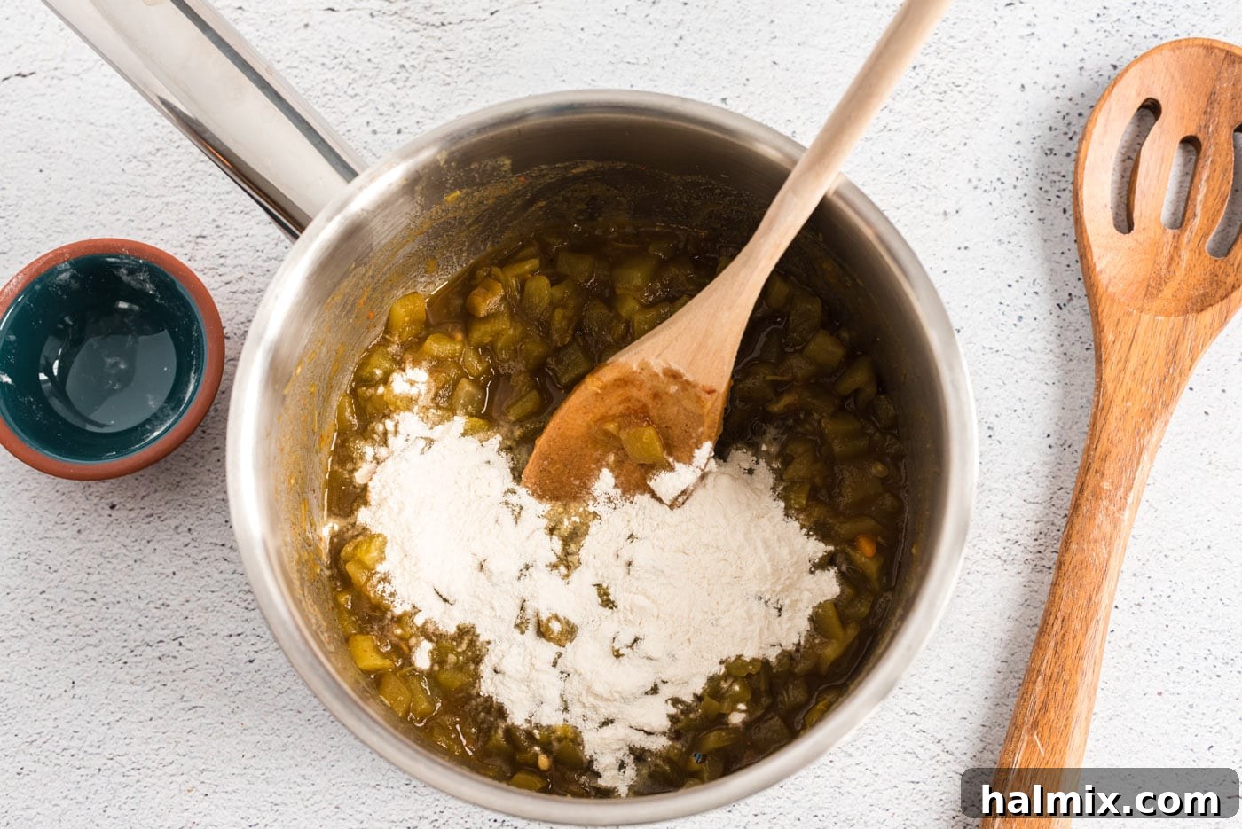 adding flour to green chiles in a saucepan
