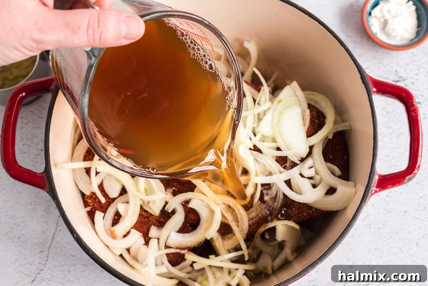 pouring broth into dutch oven with onions and chuck roast